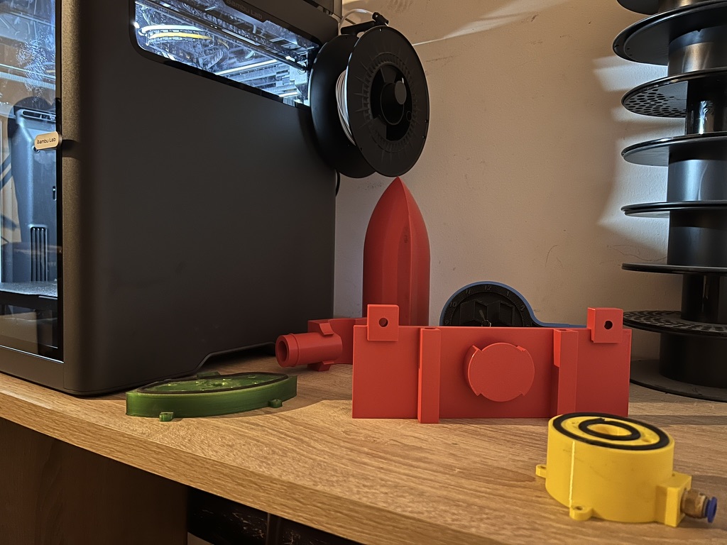 Različni 3D-tiskani izdelki na mizi ob 3D-tiskalniku